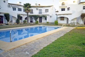 A swimming pool with a stone border, surrounded by a grassy area and a building with multiple balconies and windows. - Ap1139 in Denia With 1 Bedrooms and 1 Bathrooms (Denia)