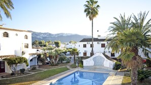 A swimming pool surrounded by white buildings with palm trees, a clear sky, and mountains in the background. - Ap1139 in Denia With 1 Bedrooms and 1 Bathrooms (Denia)