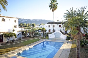 A swimming pool surrounded by white buildings with palm trees, a clear sky, and mountains in the background. - Ap1139 in Denia With 1 Bedrooms and 1 Bathrooms (Denia)