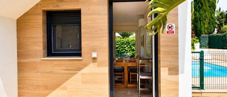 A modern building with a wooden exterior, a dining area with a table and chairs, and a pool in the background.