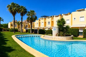 A swimming pool with a tiled edge, surrounded by a well-maintained lawn and palm trees. - Ad3202 in Denia With 3 Bedrooms and 2 Bathrooms (Denia)