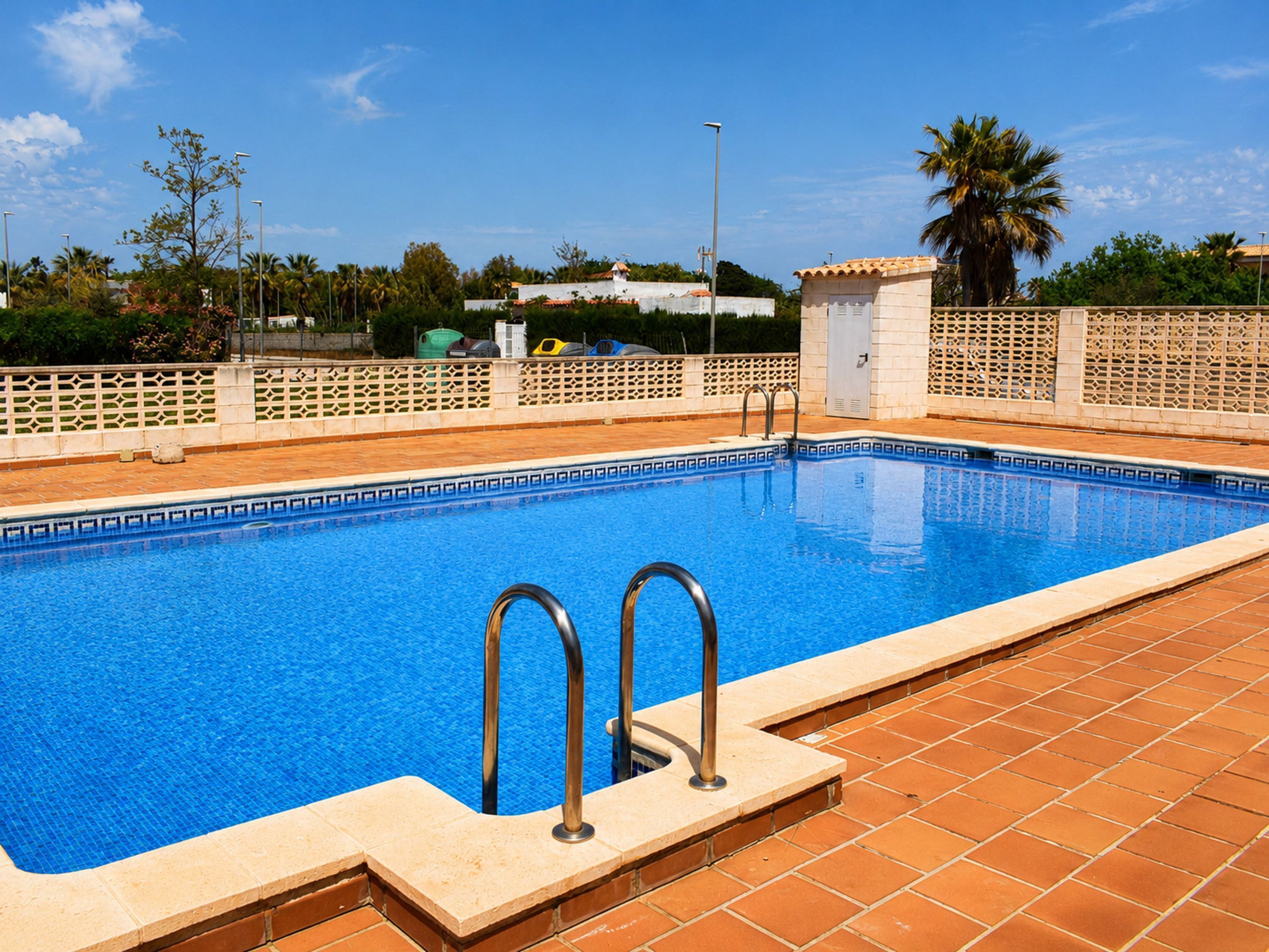 A rectangular swimming pool with a tiled edge, metal handrails, and a tiled deck surrounding it.