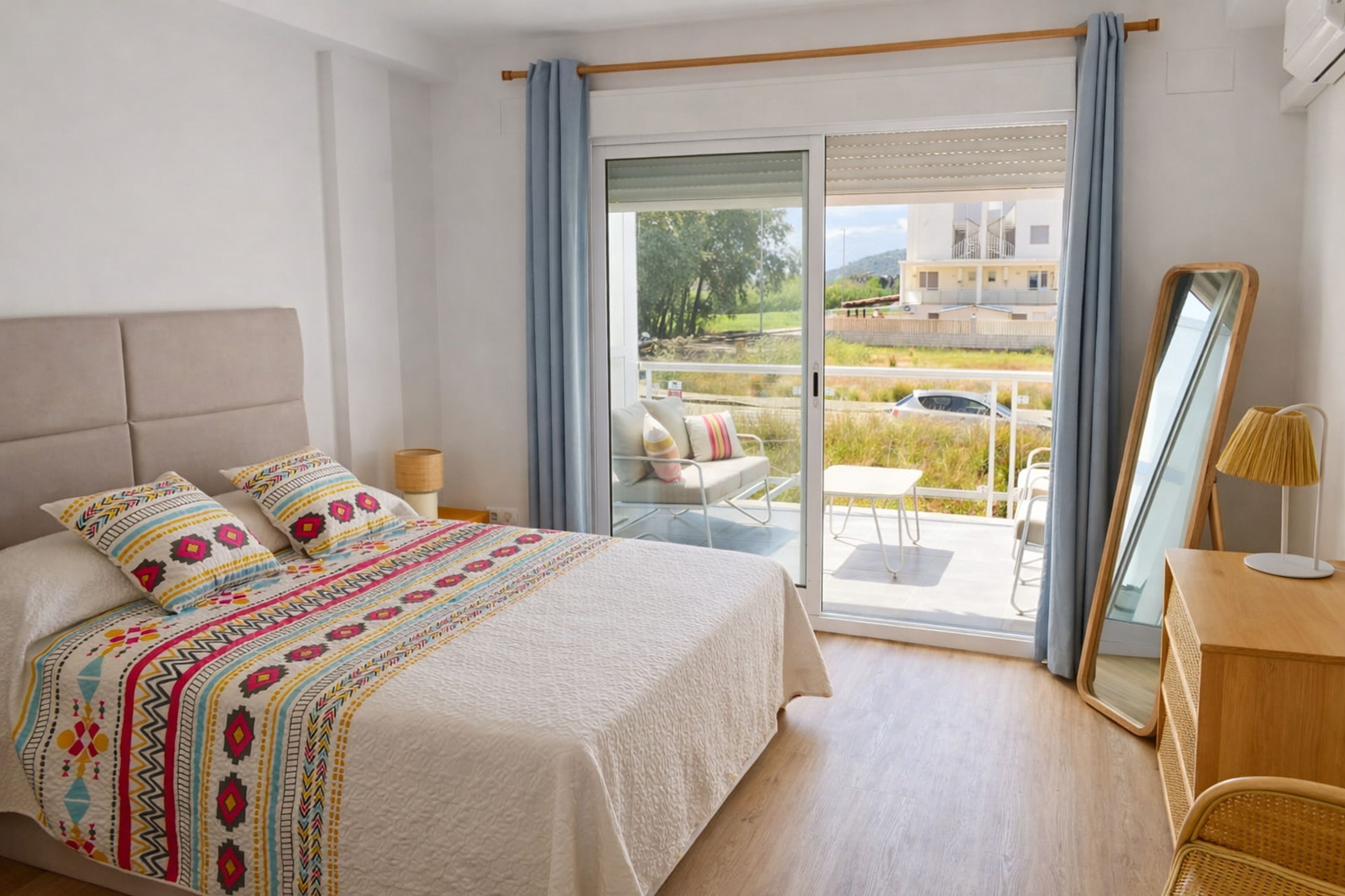 A bedroom with a bed, a nightstand, a mirror, and a view of the outdoors through a sliding door.