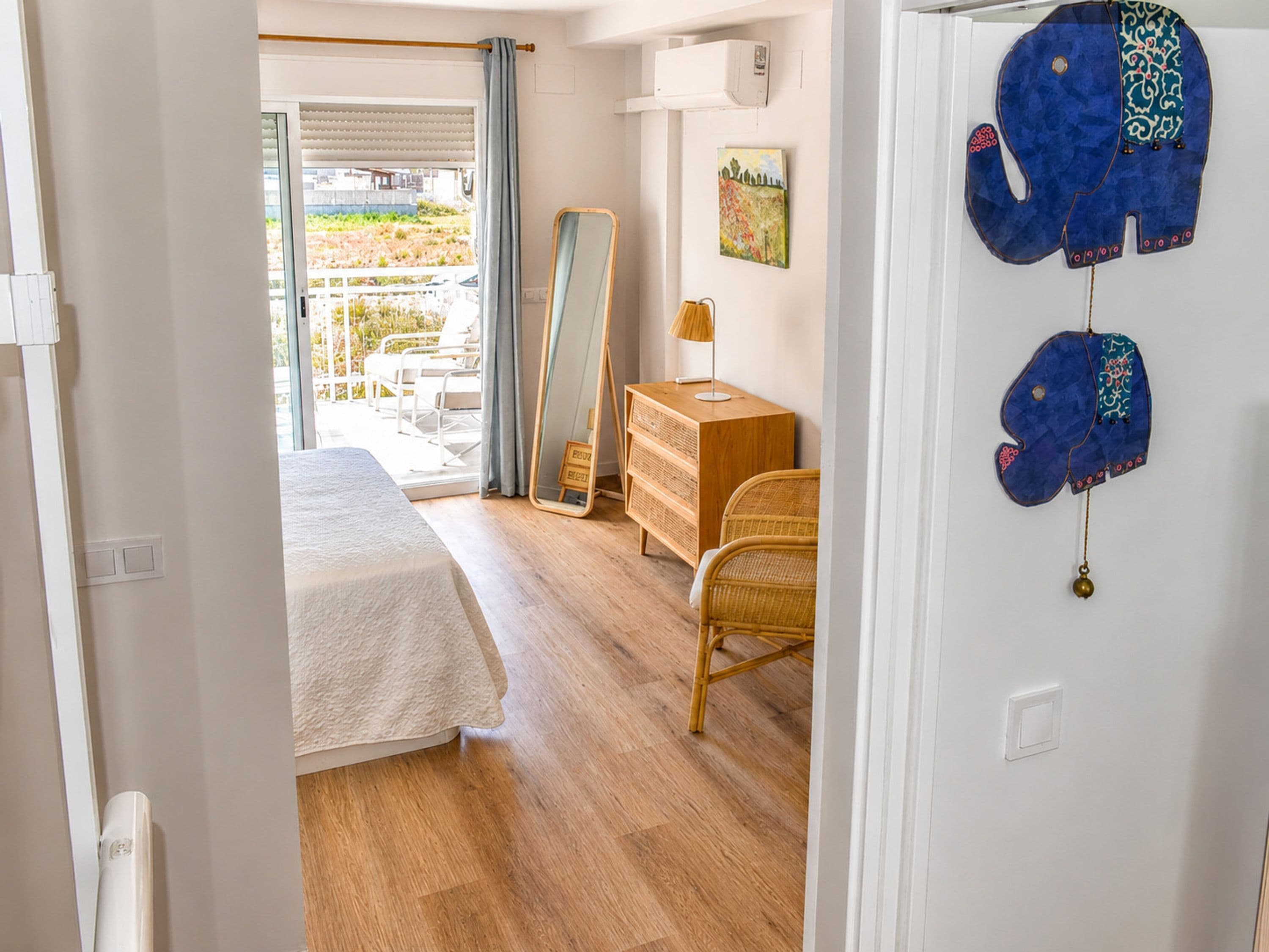 Ein Schlafzimmer mit Bett, Kommode, Spiegel und Blick ins Freie.
