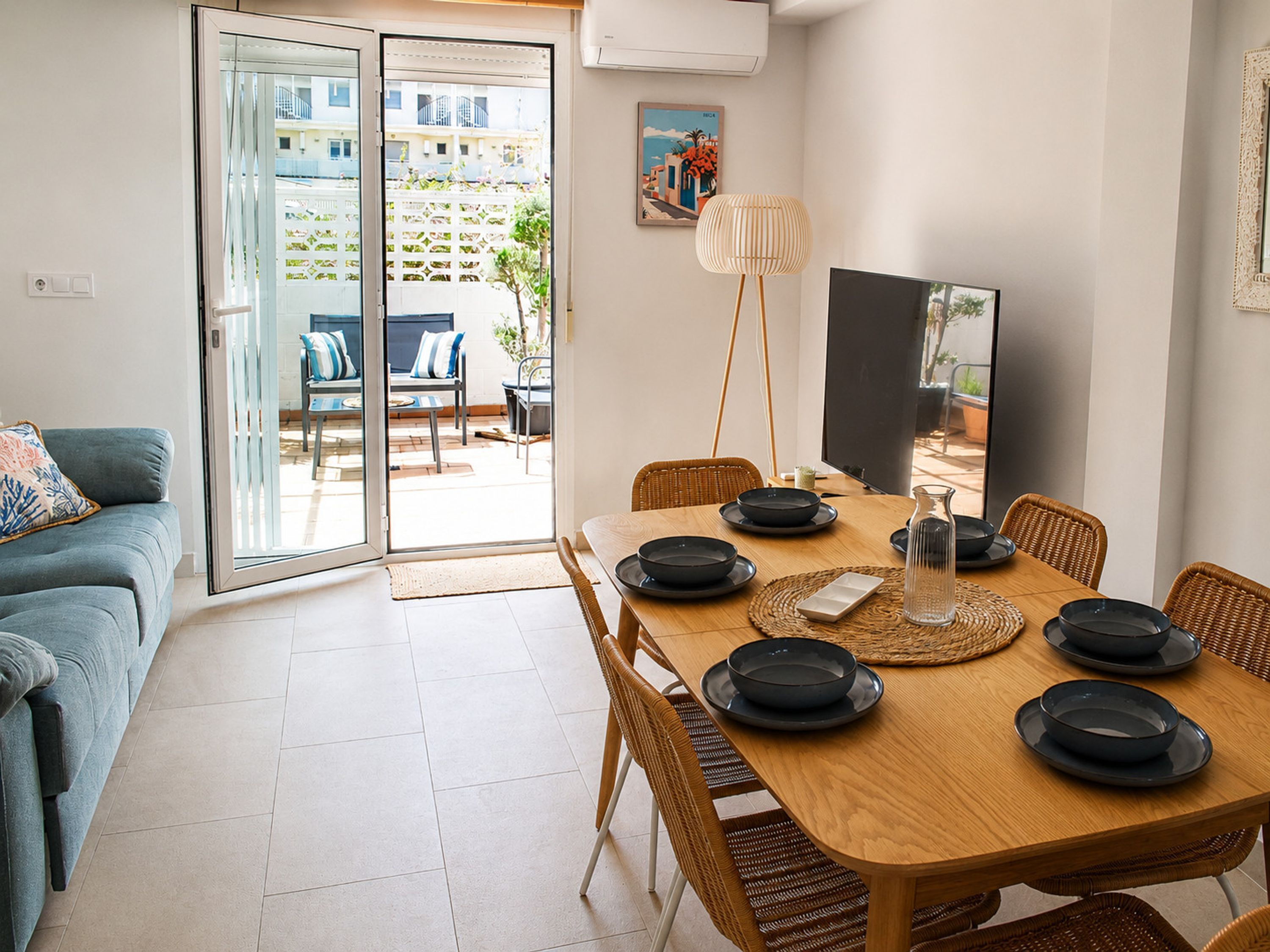 A dining area with a wooden table, black plates, wicker chairs, and a glass door leading to an outdoor patio.
