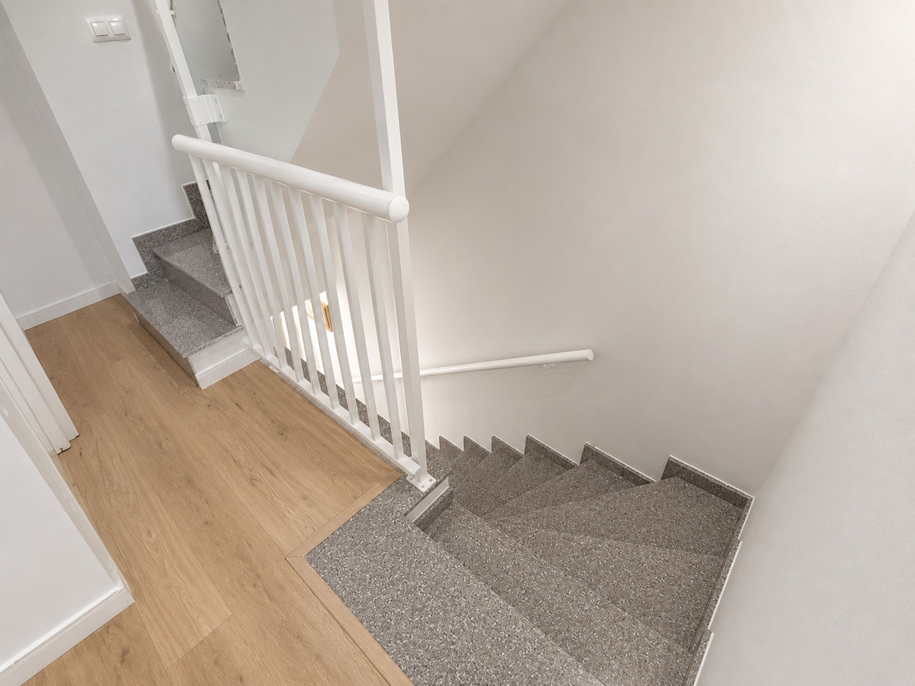 A staircase with a white handrail, wooden steps, and a grey carpeted landing.