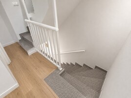 Una escalera con barandilla blanca, escalones de madera y un rellano con alfombra gris.