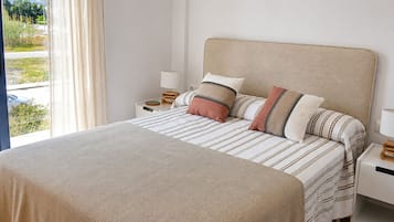 Une chambre à coucher avec un lit, des oreillers, une table de chevet, une lampe et une vue sur l’extérieur.