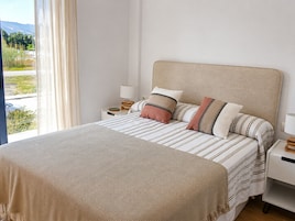Un dormitorio con cama, almohadas, una mesita de noche, una lámpara y vistas al exterior.