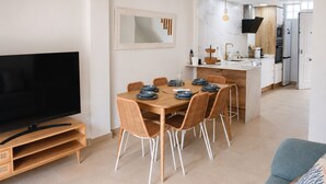 A modern living room with a flat-screen TV, a dining area with a wooden table and wicker chairs, and a kitchen with white cabinets and a built-in oven. - Ad1360 in Oliva With 3 Bedrooms and 1 Bathrooms (Oliva)