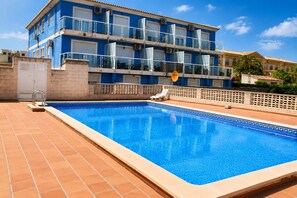 Ein Swimmingpool mit Fliesen, einem weißen Zaun und einem Gebäude mit Balkonen im Hintergrund.