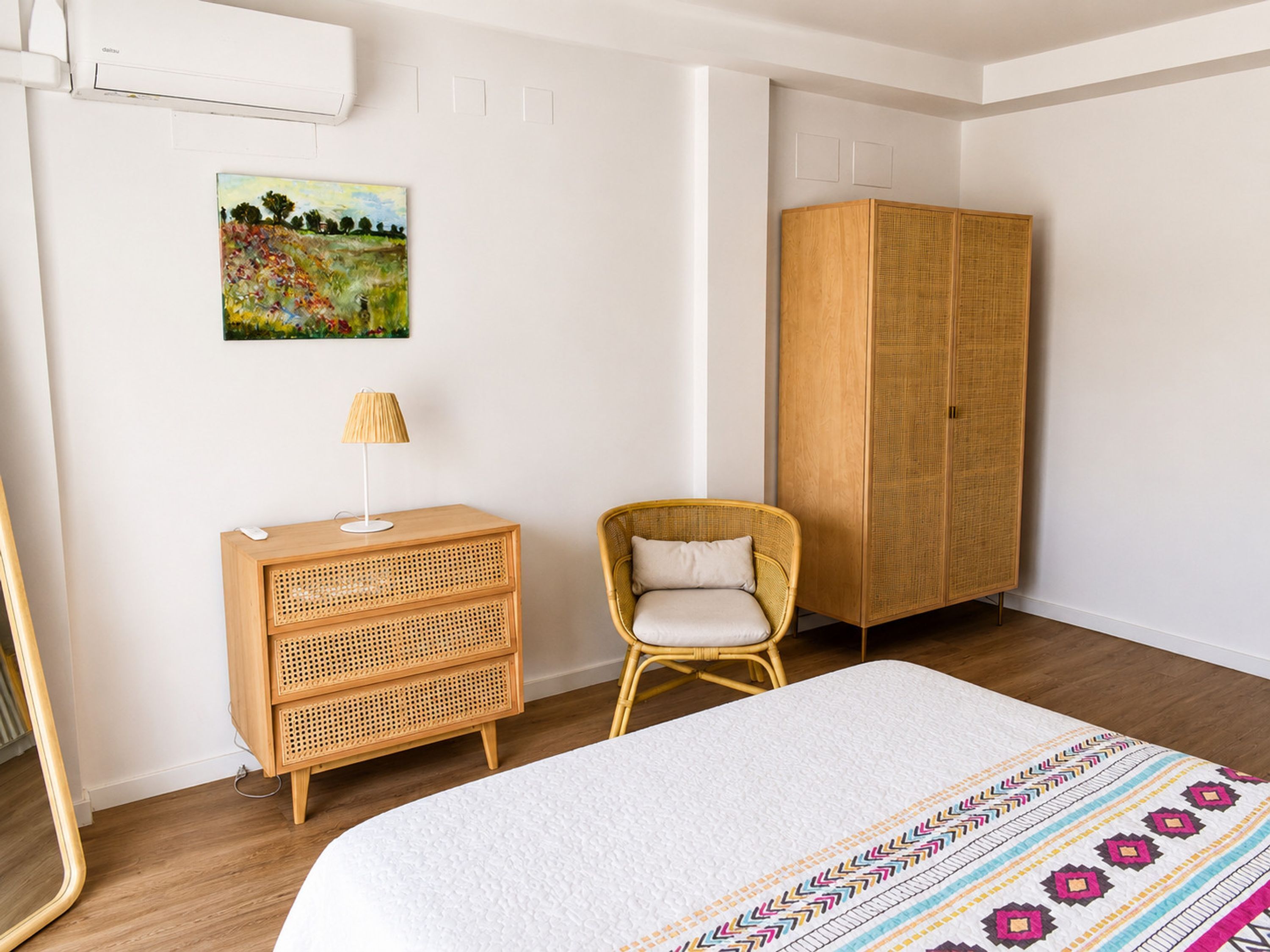 A bedroom with a bed, a wooden dresser, a wicker chair, and a wardrobe.