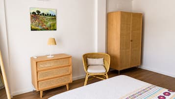 A bedroom with a bed, a wooden dresser, a wicker chair, and a wardrobe.