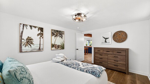 Quarto com cama, cómoda de madeira e decoração de parede incluindo a cauda de uma baleia e palmeiras.