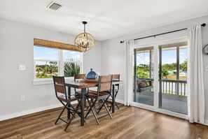 Un comedor con una mesa y sillas de madera, una lámpara colgante y vistas a través de un ventanal corredero.