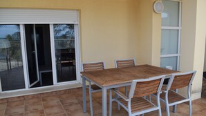 En terrasse med et træbord og stole, en skydedør i glas og en hvid væg.