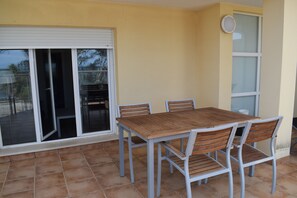 Eine Terrasse mit einem Holztisch und -stühlen, einer Schiebetür aus Glas und einer weißen Wand.