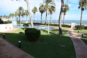 A pool area with palm trees, a clear view of the ocean, and a brick pathway. - At2202 in Denia With 2 Bedrooms and 2 Bathrooms (Denia)