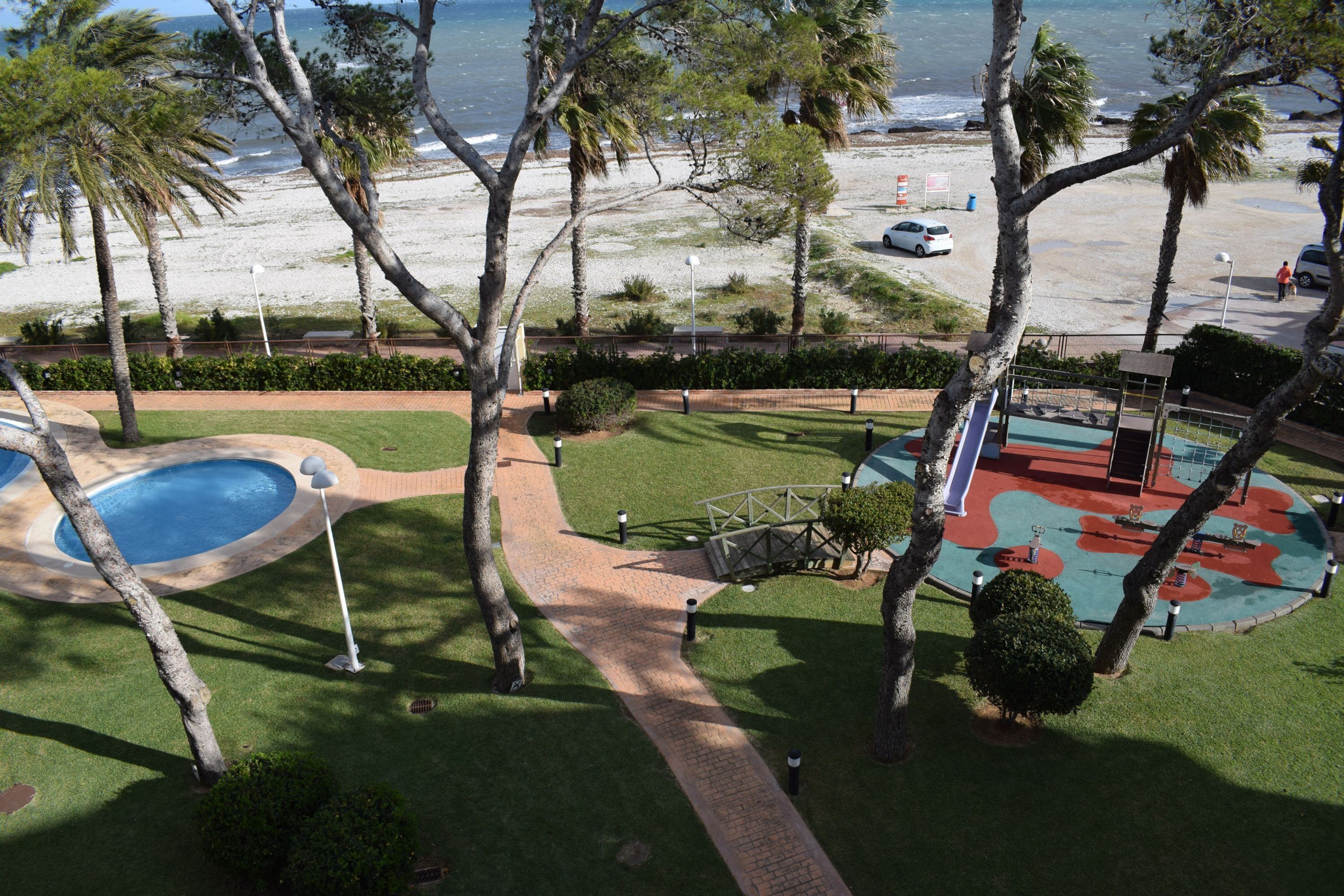 A pool area with a pathway, palm trees, and a view of the beach and ocean.