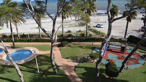 A pool area with a pathway, palm trees, and a view of the beach and ocean.