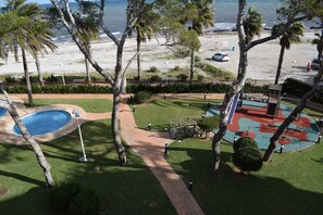 A pool area with a pathway, palm trees, and a view of the beach and ocean.