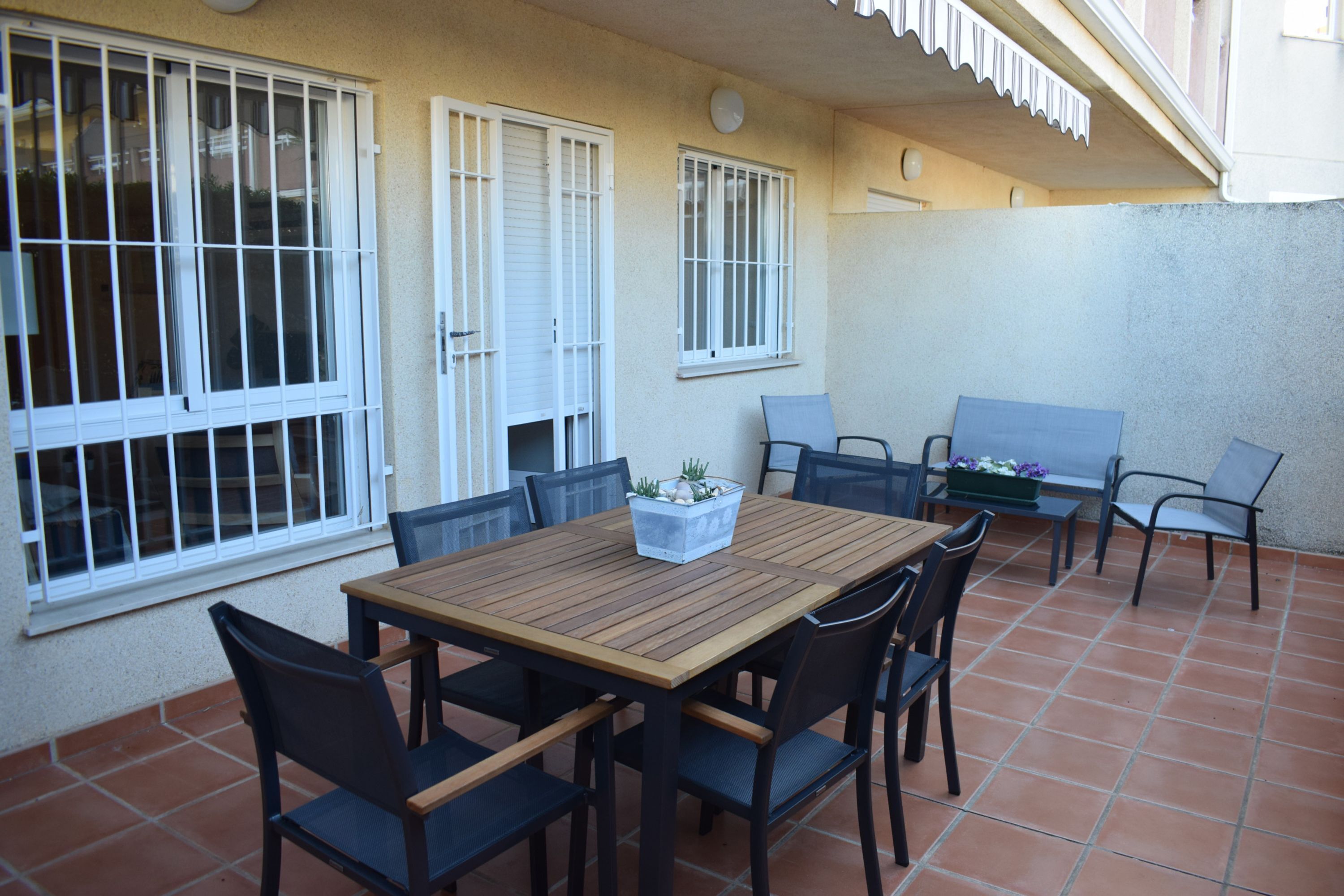 Une terrasse avec une table et des chaises en bois, une petite table avec une plante et un banc.
