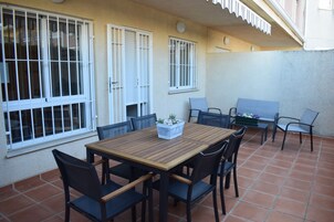 Un patio con una mesa y sillas de madera, una mesita con una planta, y un banco.