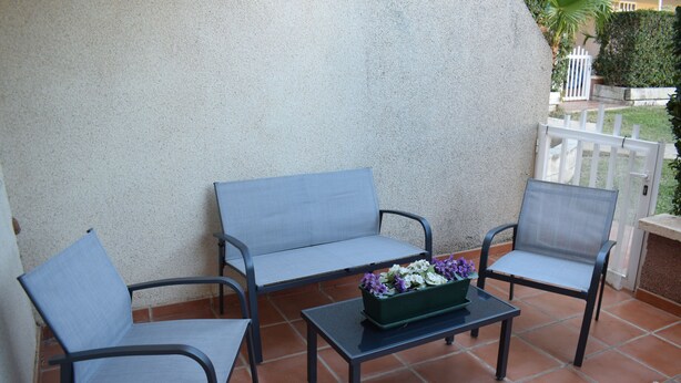 A terrace with a seating arrangement including a sofa and two chairs, a small table with a flower pot, and a white fence in the background. - Pb3201 in Denia With 3 Bedrooms and 2 Bathrooms (Denia)