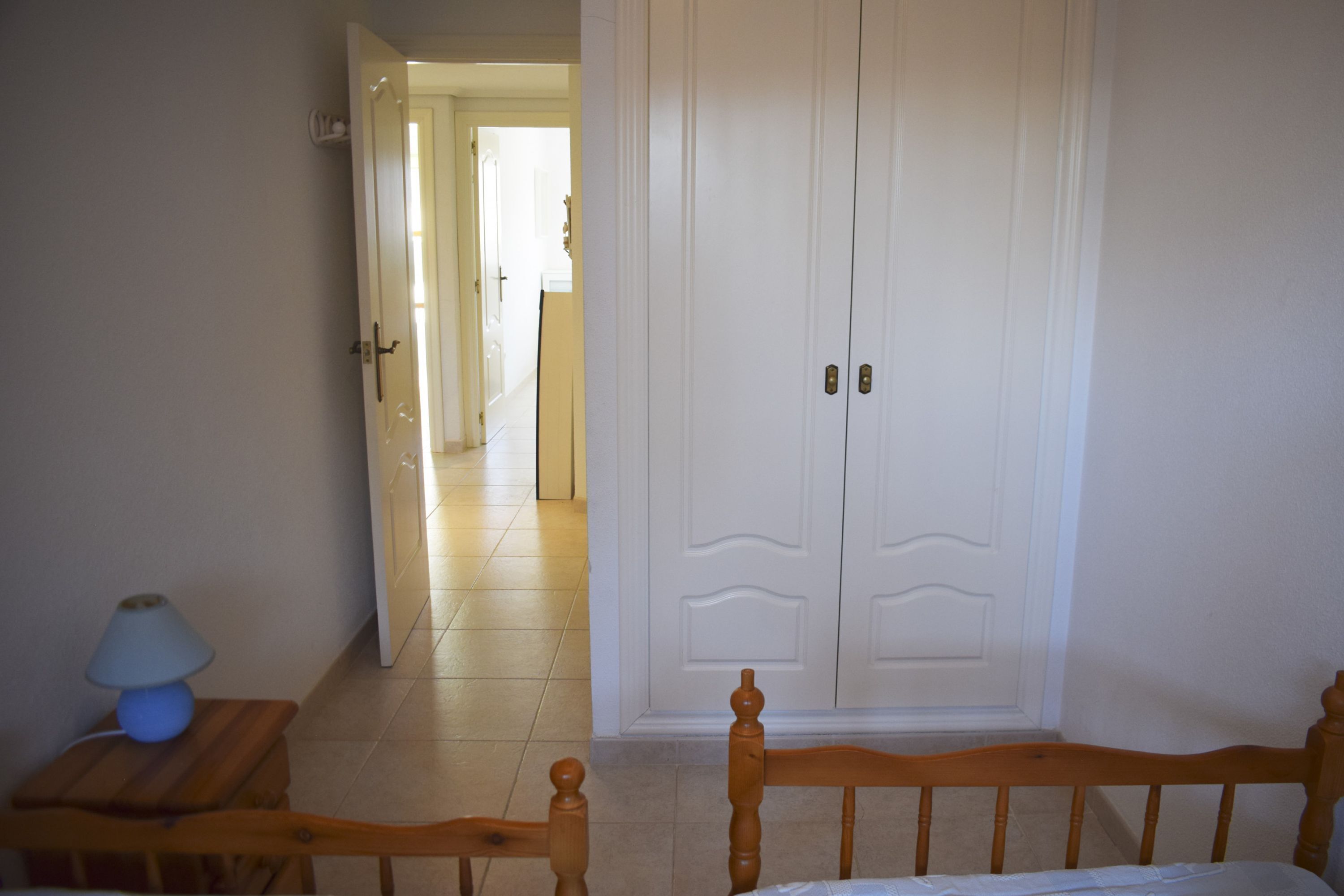 Una habitación con una cama de madera, una mesita de noche con una lámpara y un armario blanco.