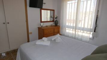 A bedroom with a bed, a dresser, a television mounted on the wall, and a window with curtains.