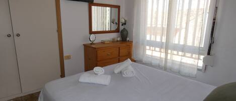 A bedroom with a bed, a dresser, a television mounted on the wall, and a window with curtains.