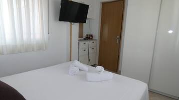 A hotel room with a bed, a television mounted on the wall, a wooden door, and a small cabinet.