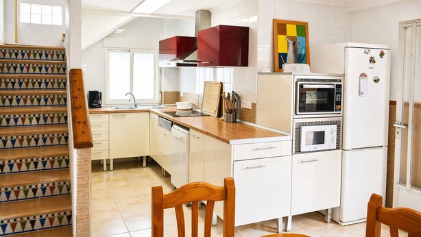 Una cocina con gabinetes blancos, una escalera de madera y piso de baldosas.