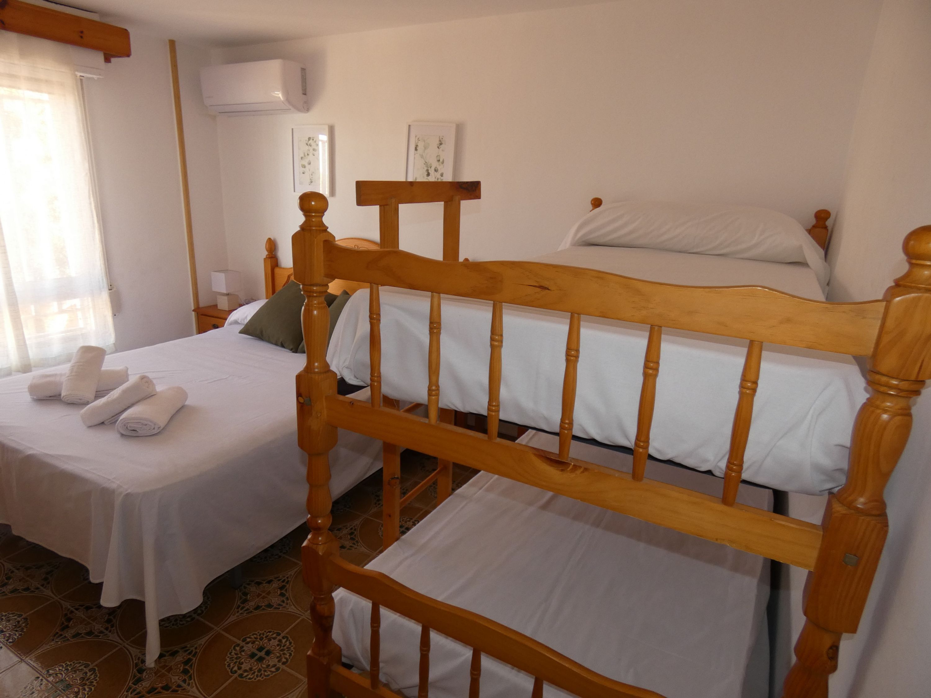 A room with two beds, one with a wooden headboard and the other with a simpler design. There are towels neatly folded on the bed with the wooden headboard.