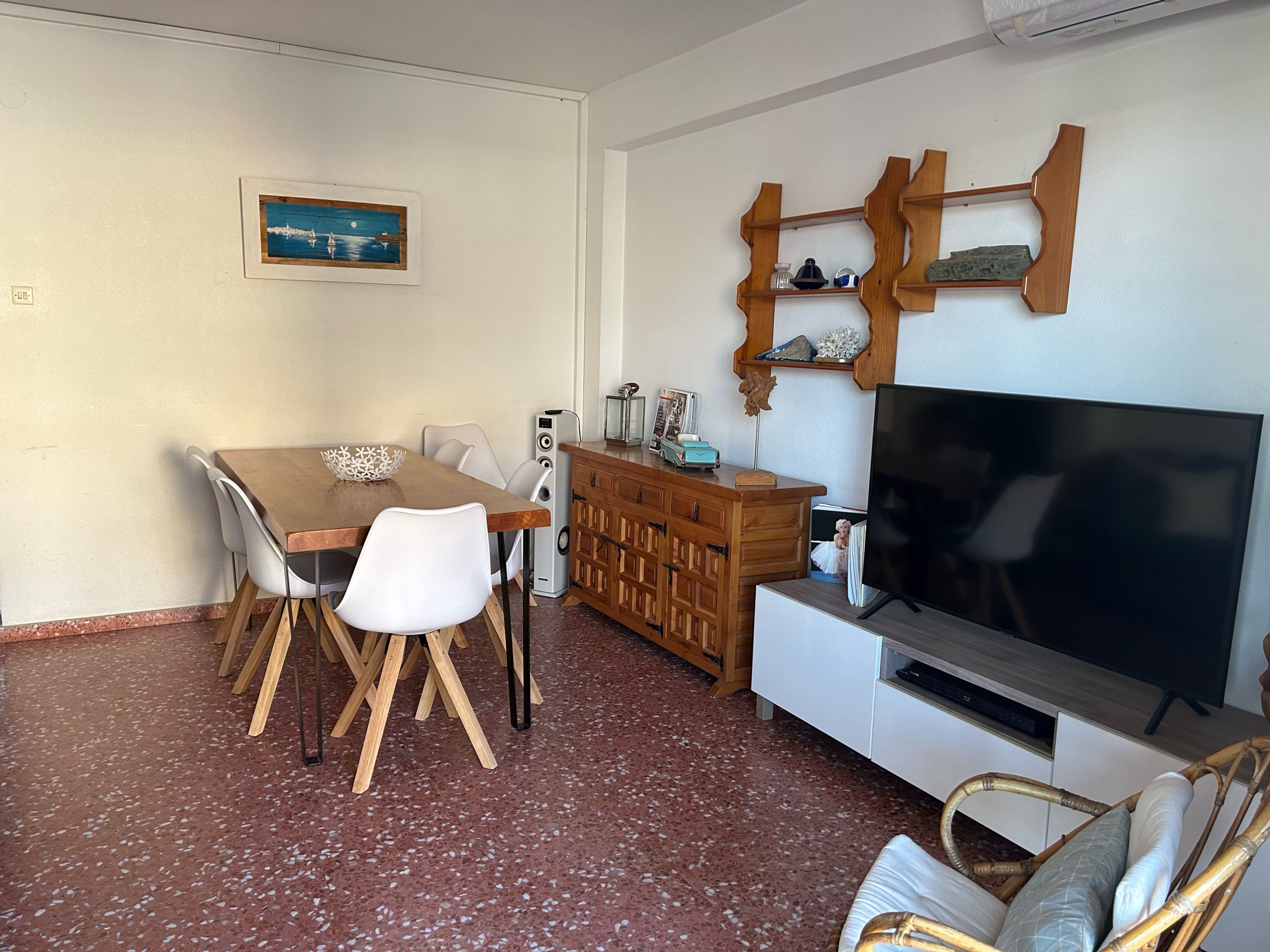 A living room with a dining table, chairs, a TV, a wooden cabinet, and a framed picture on the wall.