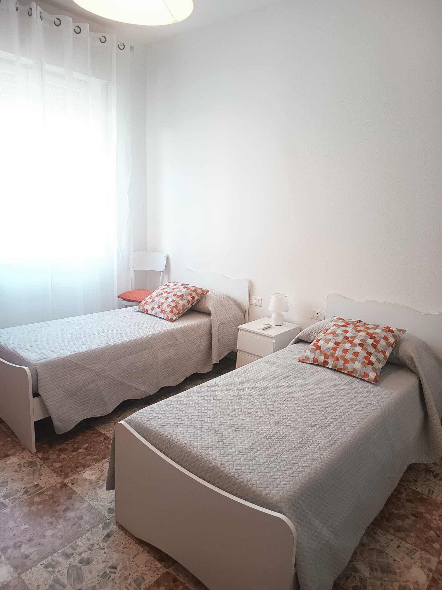 Una habitación con dos camas individuales, una mesita de noche con lámpara y una silla.