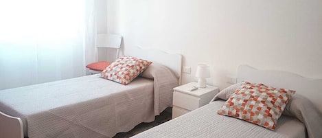 A room with two single beds, a nightstand with a lamp, and a chair.