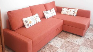 A red sectional sofa with patterned cushions in a room with a tiled floor and plain white walls. - Vada Apartment - VadaLi (Vada)