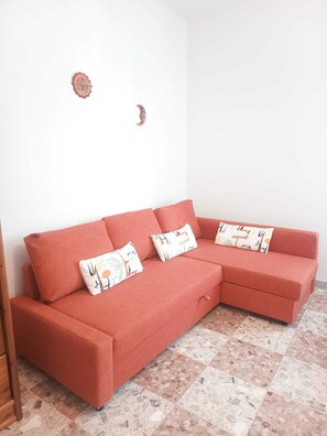 A red sectional sofa with patterned cushions in a room with a tiled floor and plain white walls. - Vada Apartment - VadaLi (Vada)