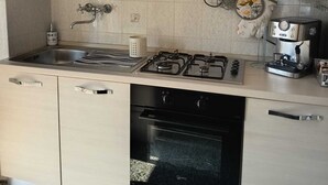 A modern kitchen with a gas stove, oven, and a coffee machine. - Vada Apartment - VadaLi (Vada)