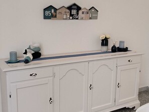 A white cabinet with three doors, a small shelf with decorative items, and a wall-mounted sign with house numbers and names. - Vada Apartment - VadaLi (Vada)