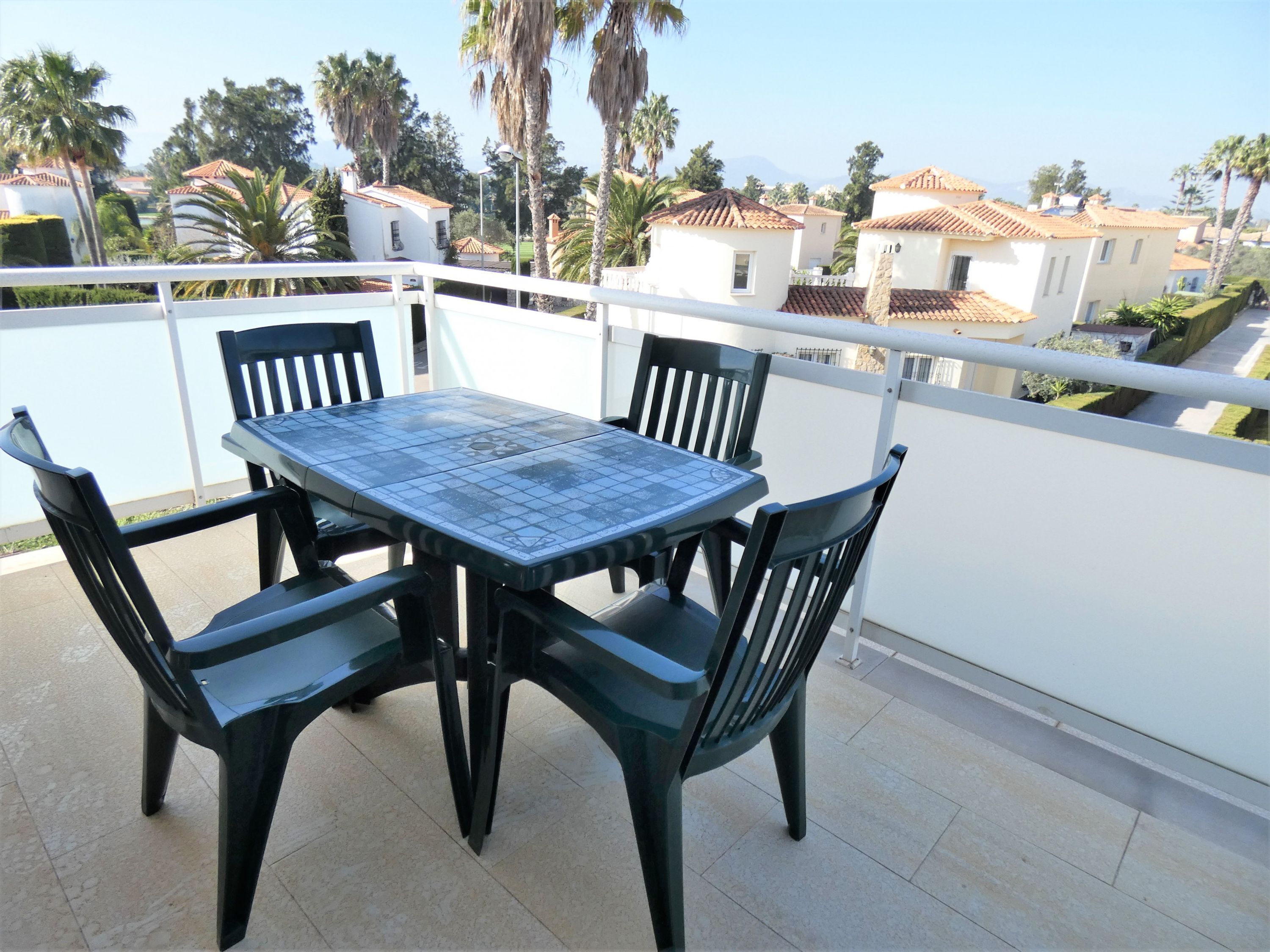 A balcony with a table and chairs, overlooking a residential area with houses and palm trees.