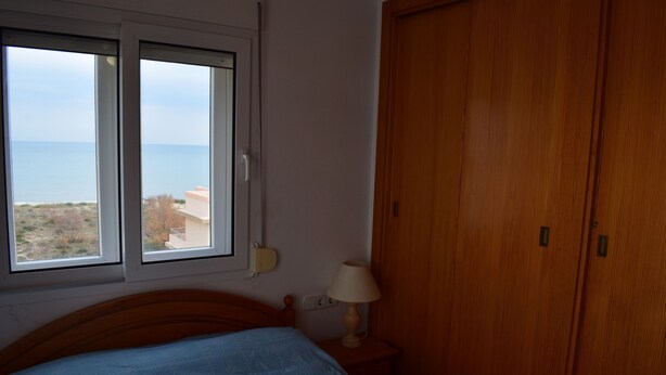Ein Schlafzimmer mit Bett, Fenster, einem Holzschrank und einer Nachttischlampe.