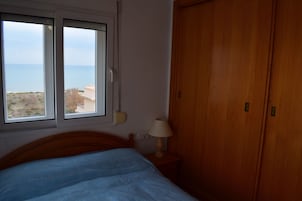 Un dormitorio con cama, ventana, armario de madera y lámpara de noche.