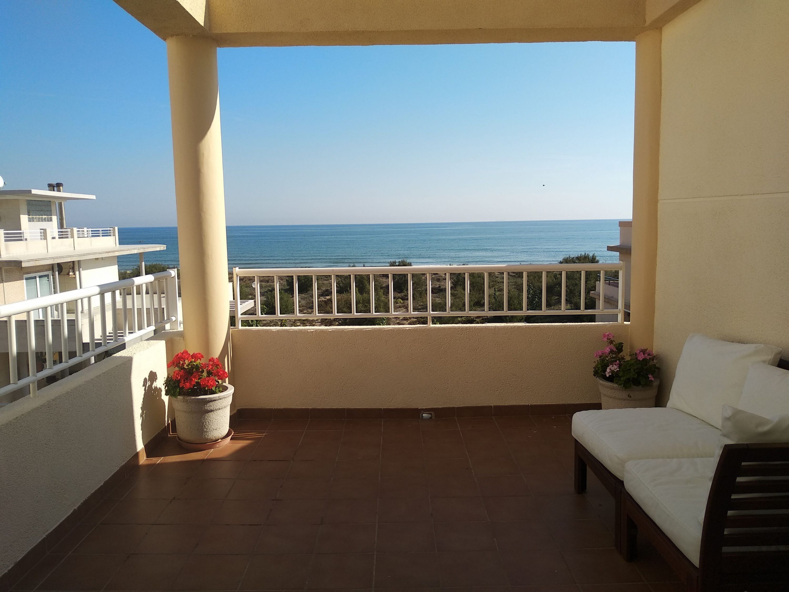 Ein Balkon mit Meerblick, ein weißes Sofa und Kübelpflanzen.