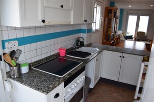 Cocina con armarios blancos, encimera de granito, placa de inducción negra, un lavabo y un cubo de basura.