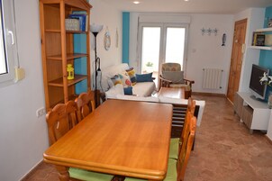Un comedor con una mesa y sillas de madera, una estantería, un sofá y un televisor sobre un mueble.