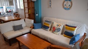 Ein Wohnzimmer mit einer Couch, einem Couchtisch und einem Holznachttisch. Im Hintergrund ist eine Küche zu sehen.