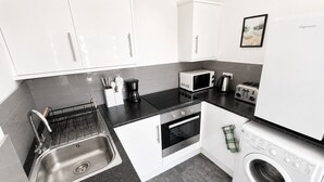 A modern kitchen with white cabinets, a stainless steel sink, a microwave, a toaster, an oven, and a washing machine. - Free Parking | Homely Gloucester Rd Flat Sleeps 3 (Bristol)