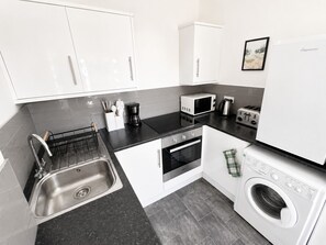 Eine moderne Küche mit weißen Schränken, einer Edelstahlspüle, einer Mikrowelle, einem Toaster, einem Backofen und einer Waschmaschine.